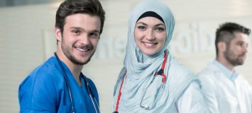 A man wearig blue scrubs with a hijab-wearing female doctor