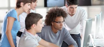 A man stares at a computer intently surrounded by a group of people watching