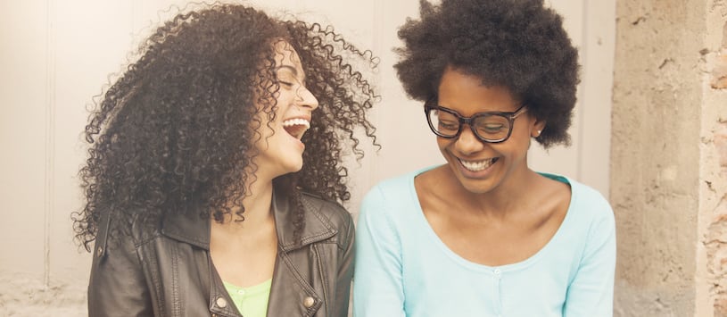 Two women of colour who are in their early twenties and hip laughing together