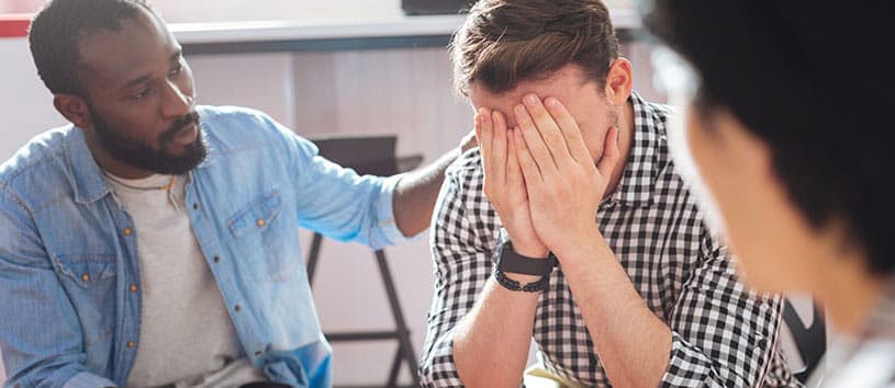 A man comforts a crying man. Take a Community Service Worker Program at Oxford College.