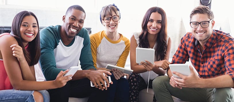 Five smiling students studying together on a couch.