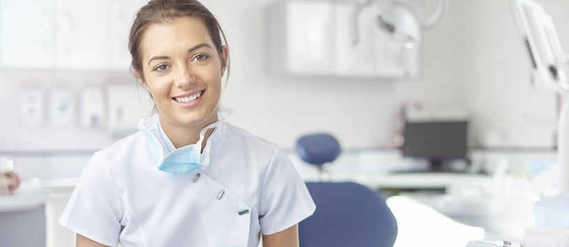 A woman wearing white scrubs with a dental chair behind